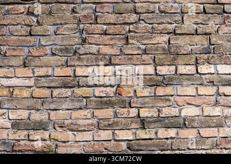 A textured brick wall is made from old, weathered bricks in various shades of brown and tan Stock Photo
