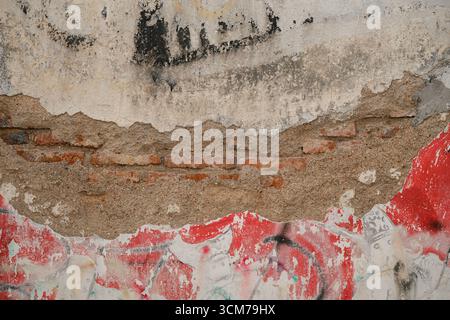 A textured wall with peeling paint, showing layers of brick and plaster, featuring red and neutral tones Stock Photo