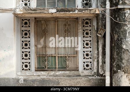 An old window with decorative metal bars and patterned concrete blocks, set against a weathered wall Stock Photo