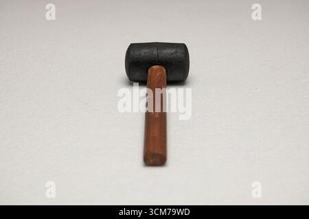 A black rubber mallet with a wooden handle, placed on a light gray surface Stock Photo