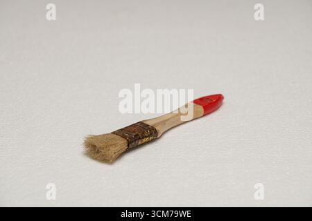 A small paintbrush with a wooden handle and red tip, featuring soft bristles, resting on a white surface Stock Photo