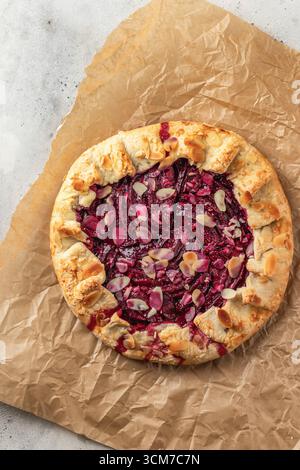 Sliced galette or pie with plums and almonds on parchment paper background top view. Summer traditional homemade sweet pastries. Vertical Stock Photo
