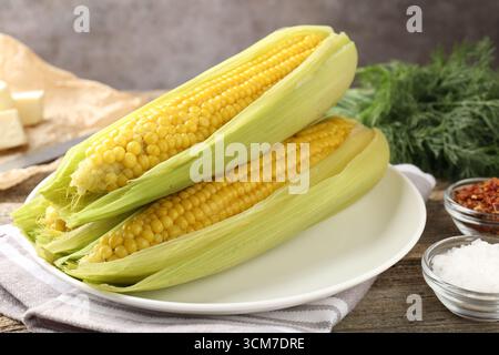 Tasty boiled corncobs, dill and spices on wooden table, closeup Stock Photo