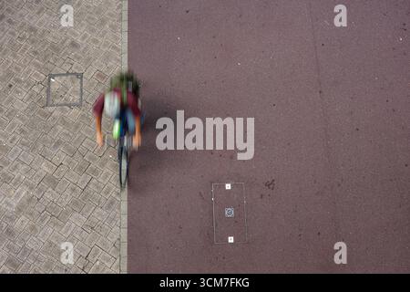 Overhead view cyclist speeding by under two-tone walkway of gray-brown paving stones and dark reddish-brown asphalt. Motion blur adds dynamic effect. Stock Photo