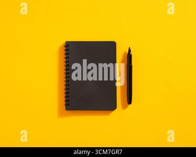 Black spiral bound notebook and pen on a yellow background, representing creativity, note-taking, and planning Stock Photo
