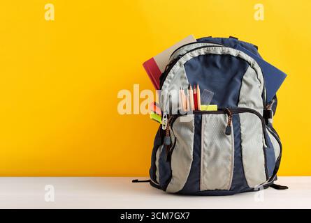 Backpack full of school supplies including notebooks, pencils, ruler and highlighters on a yellow background with copy space. Back to school concept. Stock Photo