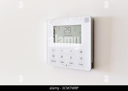 Close-up view of modern digital thermostat mounted on white wall, displaying temperature of 29C. Energy control, smart home technology, and HVAC syste Stock Photo