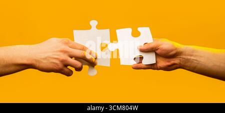 Hands connecting puzzle pieces. Male and female hand joining two matching puzzle pieces together in a conceptual image of teamwork and cooperation Stock Photo