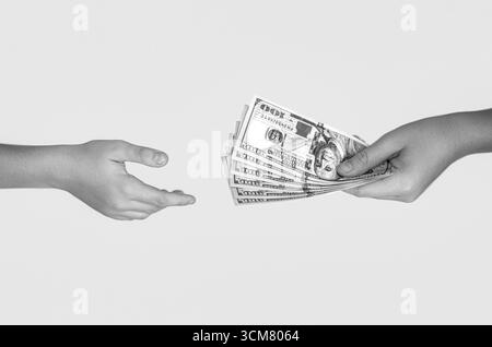 Female hand holding wad of hundred dollar cash bills passing it on to another person on gray background. Money, cash. Handing over stacks of cash to Stock Photo