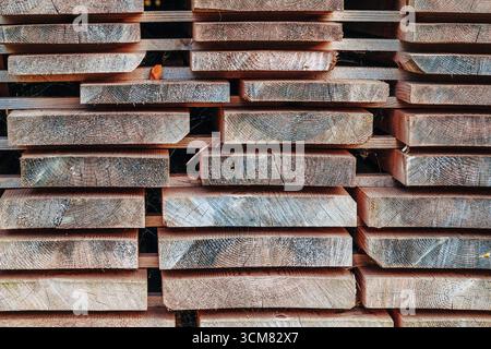 Stack of wooden planks arranged outdoors, showing natural texture and construction material for carpentry and woodworking. Stock Photo