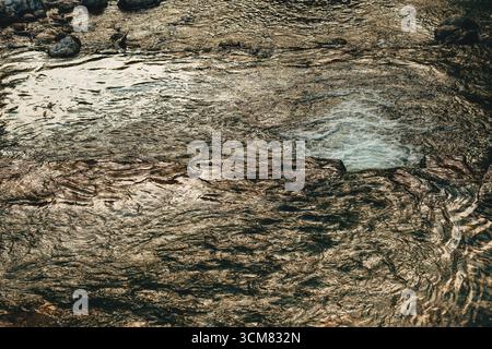 Rippled surface of a clear mountain creek with flowing water creating natural abstract patterns. High angle view. Stock Photo