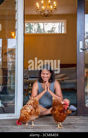 Woman sitting in the doorway of house and feeding the domestic birds Stock Photo