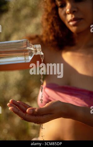 close up African American woman pouring water from bottle onto hand Stock Photo