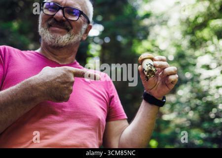 Senior smiling man with glasses holding a mushroom in a forest Stock Photo
