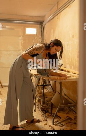 Carpenter using electric jigsaw cutting wooden plank in workshop Stock Photo