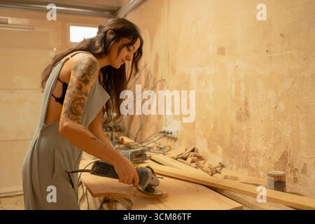 Carpenter sanding wooden plank with electric sander in workshop Stock Photo