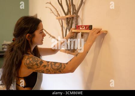 Woman installing wooden shelf using spirit level in apartment Stock Photo