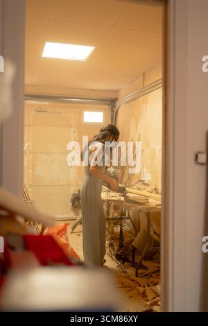 Carpenter working wood with sander in workshop wearing mask Stock Photo