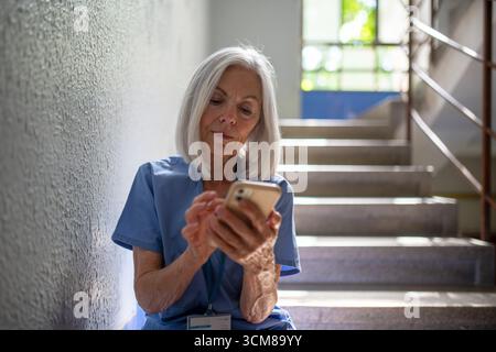 Tired nurse taking break during hospital shift, texting with family. Stock Photo