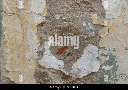 Close-up of a deteriorating plaster wall showing cracks, peeling layers, and exposed brick Stock Photo