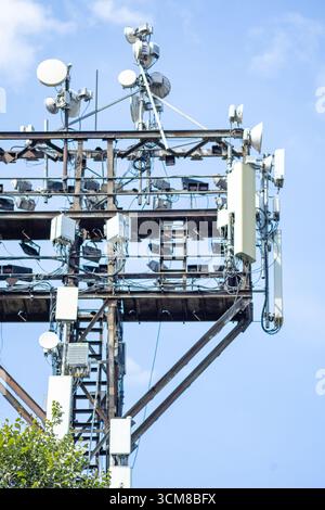 Cell tower with multiple antennas and satellite dishes against blue sky - modern communication infrastructure. Stock Photo