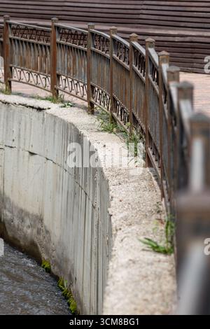 Rusty iron fence beside concrete canal bank - urban landscape with natural details Stock Photo