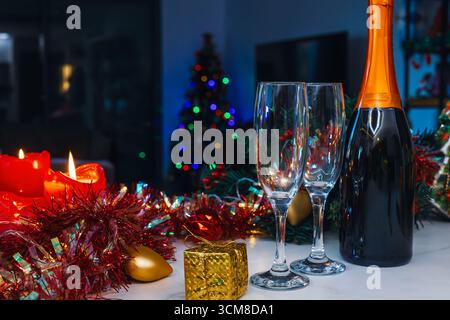 Champagne bottle and two empty glasses on a festive table with Christmas decorations and blurred tree in the background Stock Photo