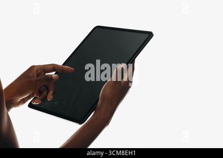 A close-up view of hands holding and interacting with a modern tablet device on a light background. Stock Photo