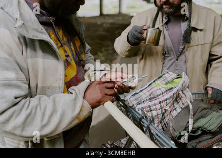 Homeless Black Man Using Mobile Phone Beside Homeless Caucasian Man Stock Photo