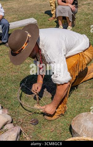 A man in period dress demonstrates using a bow & drill to start a fire at the Fort Bridger Mountain Man Rendezvous in Wyoming. Stock Photo