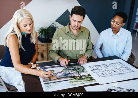 A team of professionals of different genders and age groups engaging in a design discussion, examining architectural plans in an office space, fosteri Stock Photo