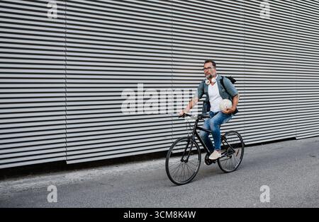 City commuter riding bike on street, wearing backpack. Looking at camera and smiling. Stock Photo