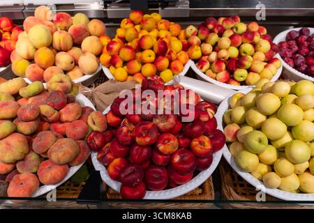 Variety of fresh peaches, nectarines, and plums displayed on market stall. Colorful summer fruits for healthy eating, organic food, and vegetarian lif Stock Photo