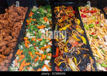 Variety of Asian-style dishes at a buffet counter, including fried chicken, stir-fried vegetables, and colorful meat dishes in stainless steel trays Stock Photo
