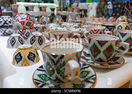 Colorful Central Asian ceramic cups, saucers, and bowls with intricate patterns and gold accents, arranged on a white surface for display Stock Photo