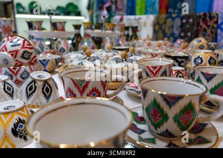 Colorful Central Asian ceramic cups, saucers, and bowls with intricate patterns and gold accents, arranged on a white surface for display Stock Photo