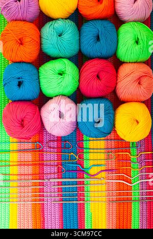 All for hand knitting. Knitted multi-colored handmade fabric with balls of multi-colored threads, pins and various knitting needles on it. Stock Photo