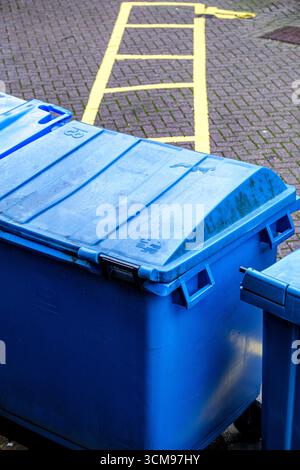 London UK September 15 2025, A Large Industrial Blue Plastic Wheelie Bin Sitting On Yellow Painted Road Markings Stock Photo