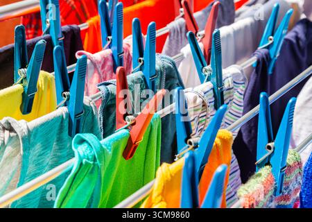 Multi-colored clothes hang attached to clothespins and dry after washing, close-up. Stock Photo