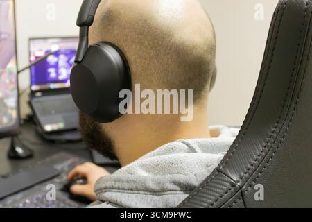 Man playing a computer game with headset, seen from behind. Desk with two monitors Stock Photo