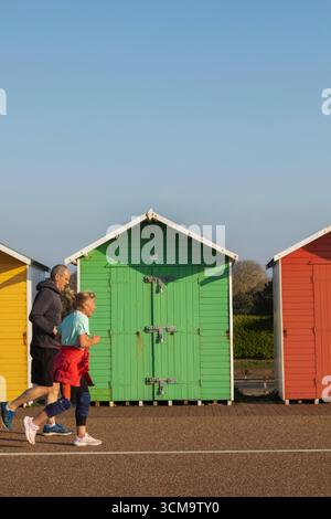 England, Sussex, East Sussex, Eastbourne, Colourful Beach Huts on the Beachfront, Elderly Couple Jogging Stock Photo