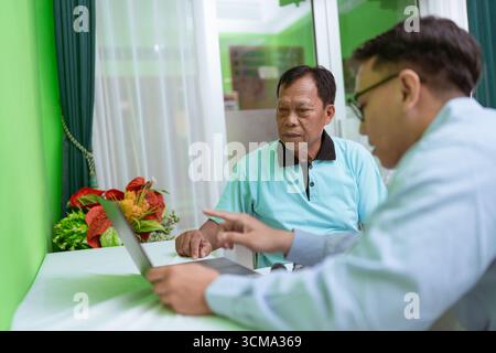 Two Men Working Together on a Laptop in the Comfort of Home with a Green Background Stock Photo
