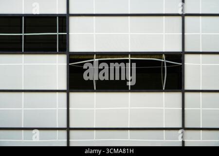 Unexpected Distortions: The Curved Echoes. A facade in Stockholm, Sweden shows strict black grid lines contrasted with white curved reflections on glass panes, where surrounding distortions break the geometry and add dynamic complexity to the modern design. Stock Photo