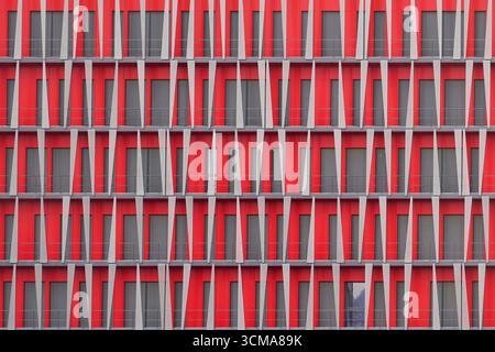 Urban Checkerboard: Rhythmic Pattern. A facade in Grenoble, France, designed by SOHO Architects Lyon, shows bold red panels with gray shutters arranged in a checkerboard rhythm. The alternating shutters add individuality within the geometric uniformity. Stock Photo