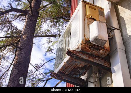 An old and rusty air conditioner hanging on the hotel building, in the sunny outdoor, seaside resort Stock Photo