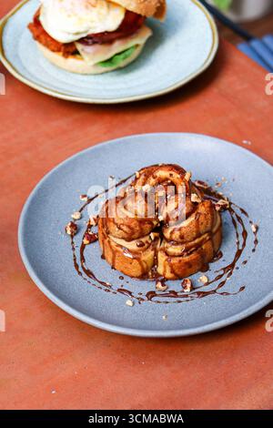 golden cinnamon rolls are drizzled with a rich chocolate or caramel sauce and topped with crunchy chopped nuts. Brunch scene Stock Photo
