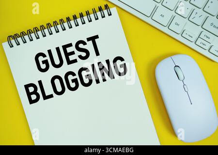 Notepad with the text "Guest Blogging" with white keyboard and wireless mouse on yellow background Stock Photo
