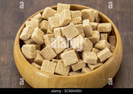 An organic brown sugar cubes in wooden bowl rustic style natural sweetener healthy ingredient close up textured surface kitchen table cozy atmosphere Stock Photo