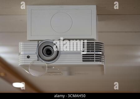 Modern white ceiling mounted projector with lens cap in contemporary interior. Smart home technology, innovation and home cinema experience Stock Photo