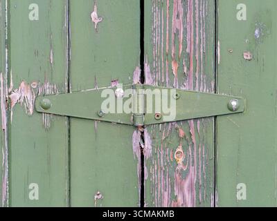 Peeling green paint on a wooden panelled gate with green painted metal hinge Stock Photo